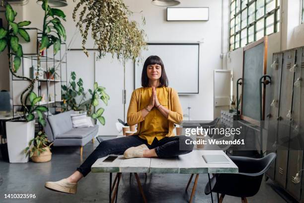 businesswoman meditating with hands clasped on desk at workplace - office yoga stock pictures, royalty-free photos & images