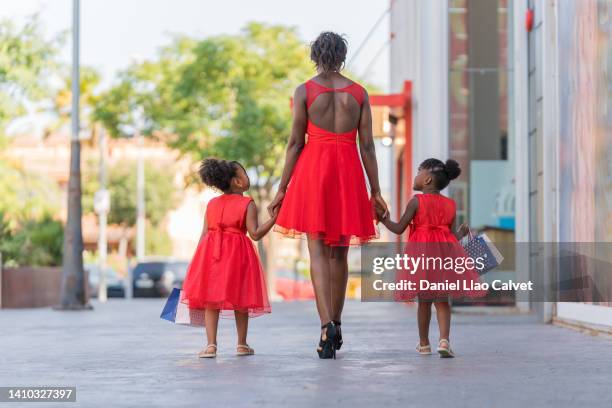 rear view of an african american mother and daughters walking on street during a shooping day - vestido rojo stock-fotos und bilder