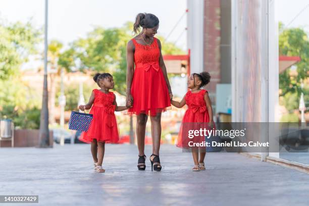 african american mother and daughters walking on street during a shooping day - vestido rojo stock-fotos und bilder