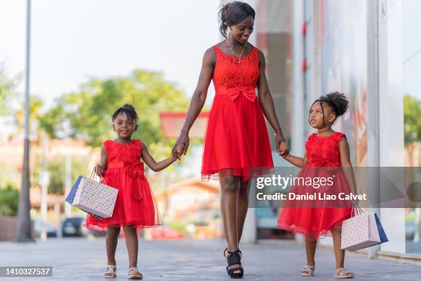 mother and daughters walking on street during a shooping day - vestido rojo stock-fotos und bilder