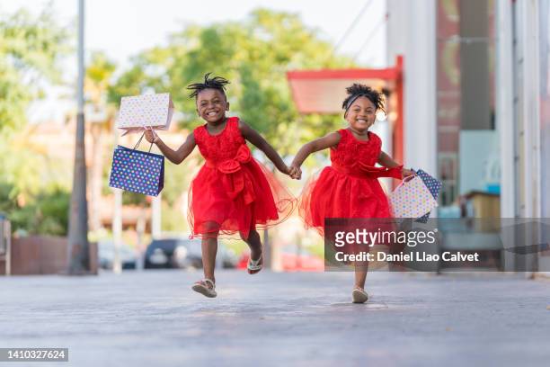 4 year old african american girls running with shopping bags towards their mother. - vestido ストックフォトと画像