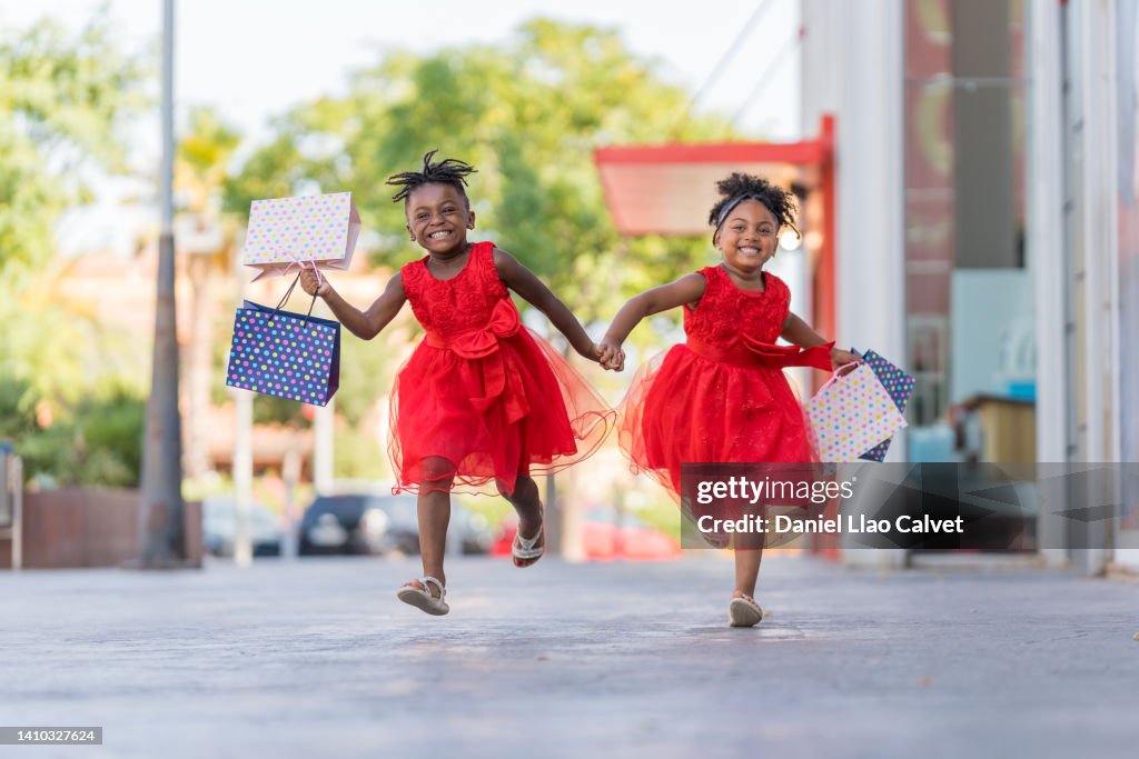 4 year old African American girls running with shopping bags towards their mother.
