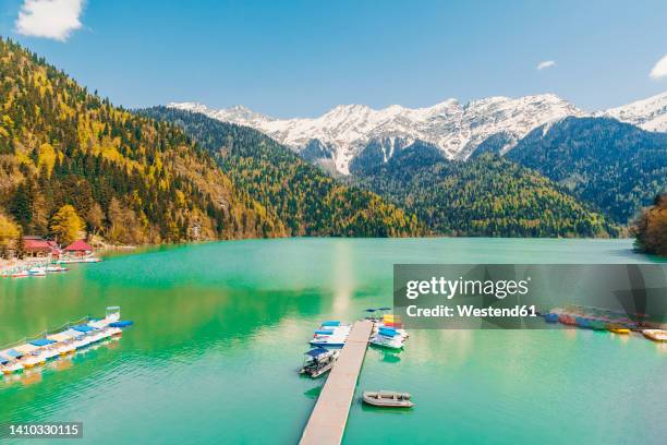 boats moored by jetty at lake ritsa on sunny day - abkhazia stock-fotos und bilder