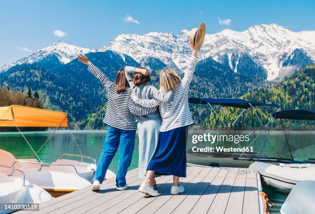 friends standing with arms around each other in front of mountains at lake ritsa - abkhazia stock pictures, royalty-free photos & images