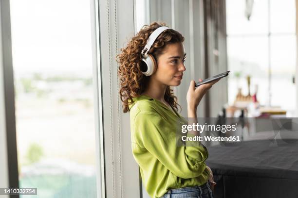 businesswoman with headphones talking on speaker phone near window at office - auscultador equipamento áudio imagens e fotografias de stock