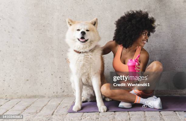 smiling woman with water bottle sitting by dog on exercise mat - curly dog stock pictures, royalty-free photos & images