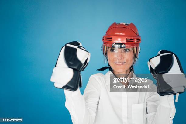 businesswoman wearing gloves and helmet against blue background - guante de hockey sobre hielo fotografías e imágenes de stock