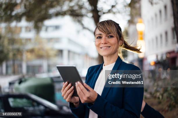 smiling businesswoman with tablet pc on street - tossing hair facing camera woman outdoors stock-fotos und bilder