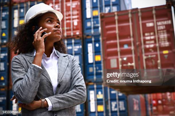 portrait tanned woman in factory at container yard, yong woman wearing safety helmet  standing business discussion at container year,  logistic business and supply chain concept - cultures meeting stock pictures, royalty-free photos & images