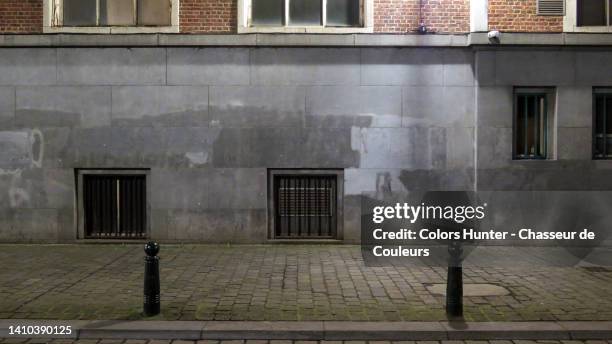 weathered gray stone and brick wall with opaque windows and cobbled sidewalk at night in brussels, belgium - street wall stockfoto's en -beelden