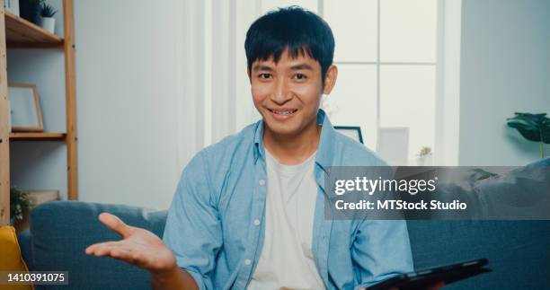 young man looking at camera making video call with customer sitting on sofa in living room at home. - webcam photo stock pictures, royalty-free photos & images