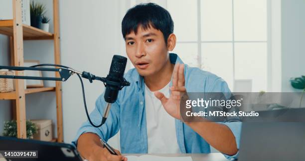 young man recording a podcast on her laptop computer with a microscope sitting at work desk in living room at home. - male influencer stock pictures, royalty-free photos & images
