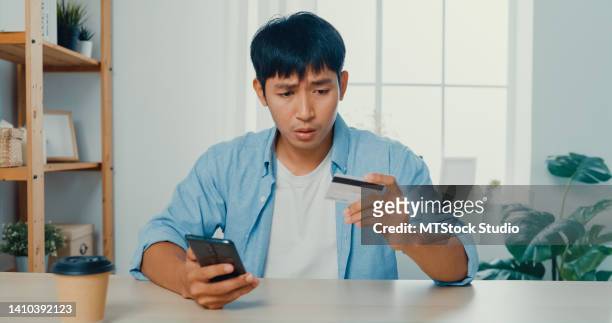 jeune homme utilisant un téléphone et une carte de crédit pour faire des achats en ligne assis à un bureau dans le salon à la maison. - phone credit card photos et images de collection
