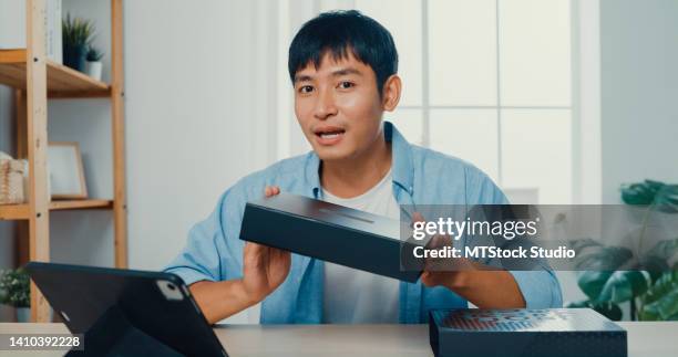 young man blogger opening parcel box and recording unboxing video with camera sitting at work desk in living room at home. - vinyl film stockfoto's en -beelden