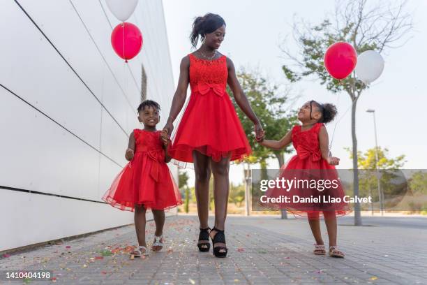 african family dressed in red and carrying colorful balloons, walking hand in hand. - vestido rojo stock-fotos und bilder