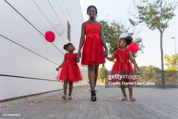 family dressed in red and carrying colorful balloons, walking hand in hand. - vestido stock pictures, royalty-free photos & images