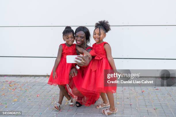 a single mom having fun with her two daughters, while taking selfies on her smartphone. - vestido rojo stock-fotos und bilder