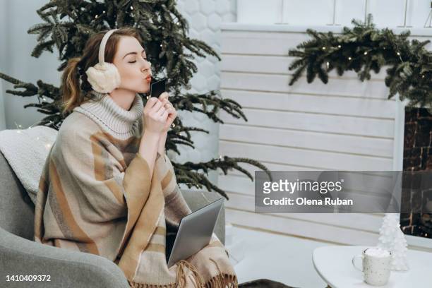 young woman kissing credit card in chair against xmas tree. - earmuffs foto e immagini stock