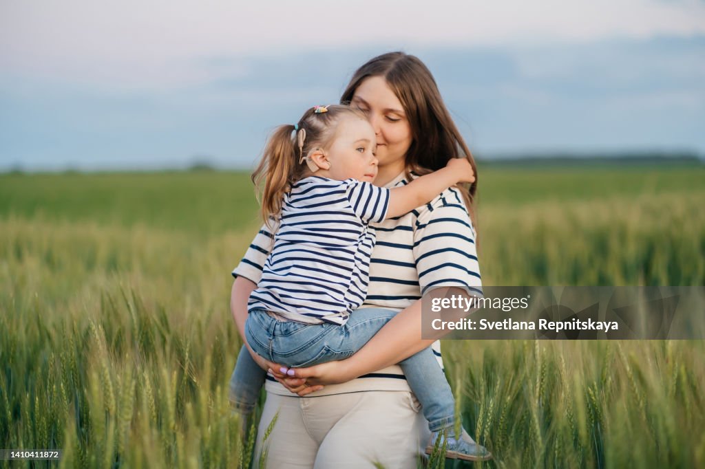 Mom hugging daughter with cochlear implant in wheat field