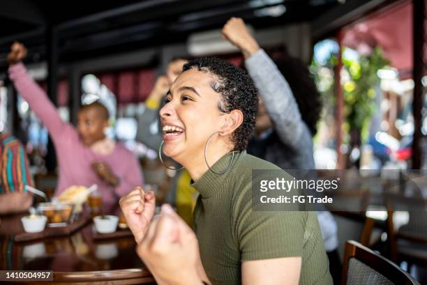 young sports fan woman watching a match with friends and celebrating in a bar - basketball match on tv stockfoto's en -beelden