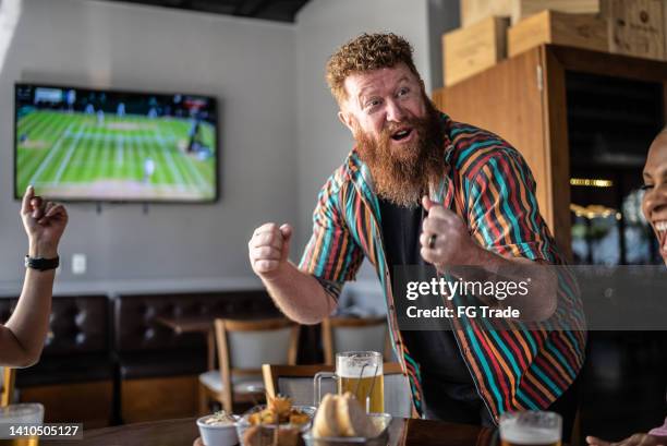 mature man celebrating with friends while watching sports at a bar - tennis game stock pictures, royalty-free photos & images