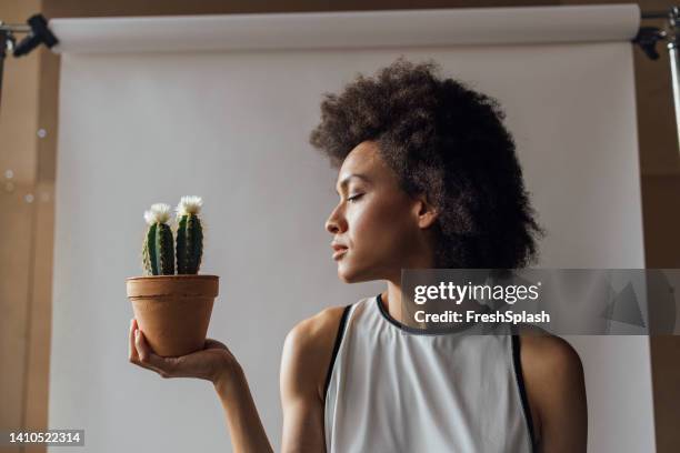 una mujer seria sosteniendo un cactus y mirándolo - flower arm fotografías e imágenes de stock