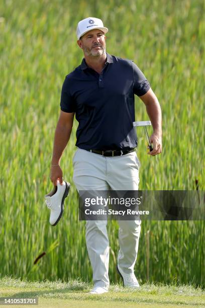 Scott Piercy of the United States walks across the 10th green while holding one of his shoes during the third round of the 3M Open at TPC Twin Cities...