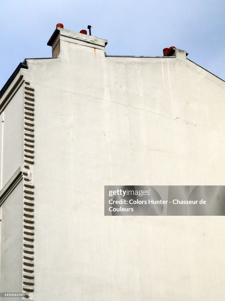 Partially and slightly sideways view of the white painted gable with chimney of a house with sky in Paris, France