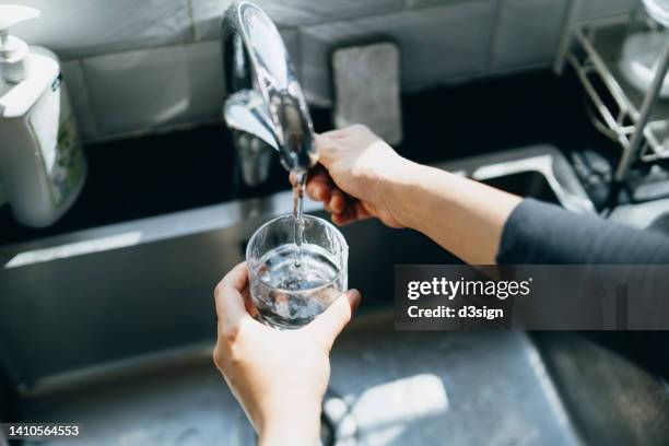 cropped shot of woman's hand filling a glass of filtered water right from the tap in the kitchen sink at home - eau courante photos et images de collection