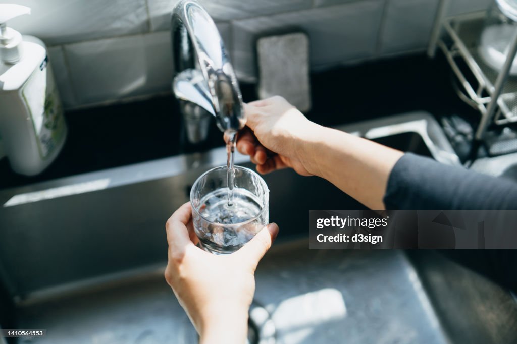 Cropped shot of woman's hand filling a glass of filtered water right from the tap in the kitchen sink at home