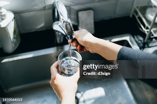 Cropped shot of woman's hand filling a glass of filtered water right from the tap in the kitchen sink at home Cropped shot of woman's hand filling a glass of filtered water right from the tap in the kitchen sink at home