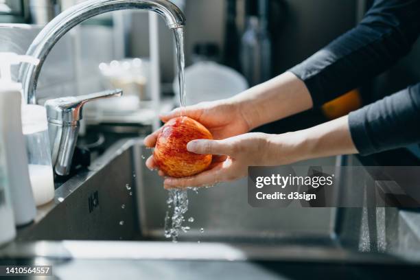 cropped shot of woman's hand washing an red apple with running water in the kitchen sink at home - lavar imagens e fotografias de stock
