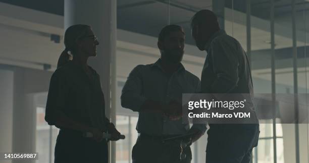 silhouette of three people inside a dark empty office building or warehouse. low angle of unrecognizable workers and manager standing, planning remodel layout or discussing construction - building low angle stock pictures, royalty-free photos & images