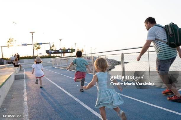 father running with his three children along the evening sunny beach - the runaways photos et images de collection