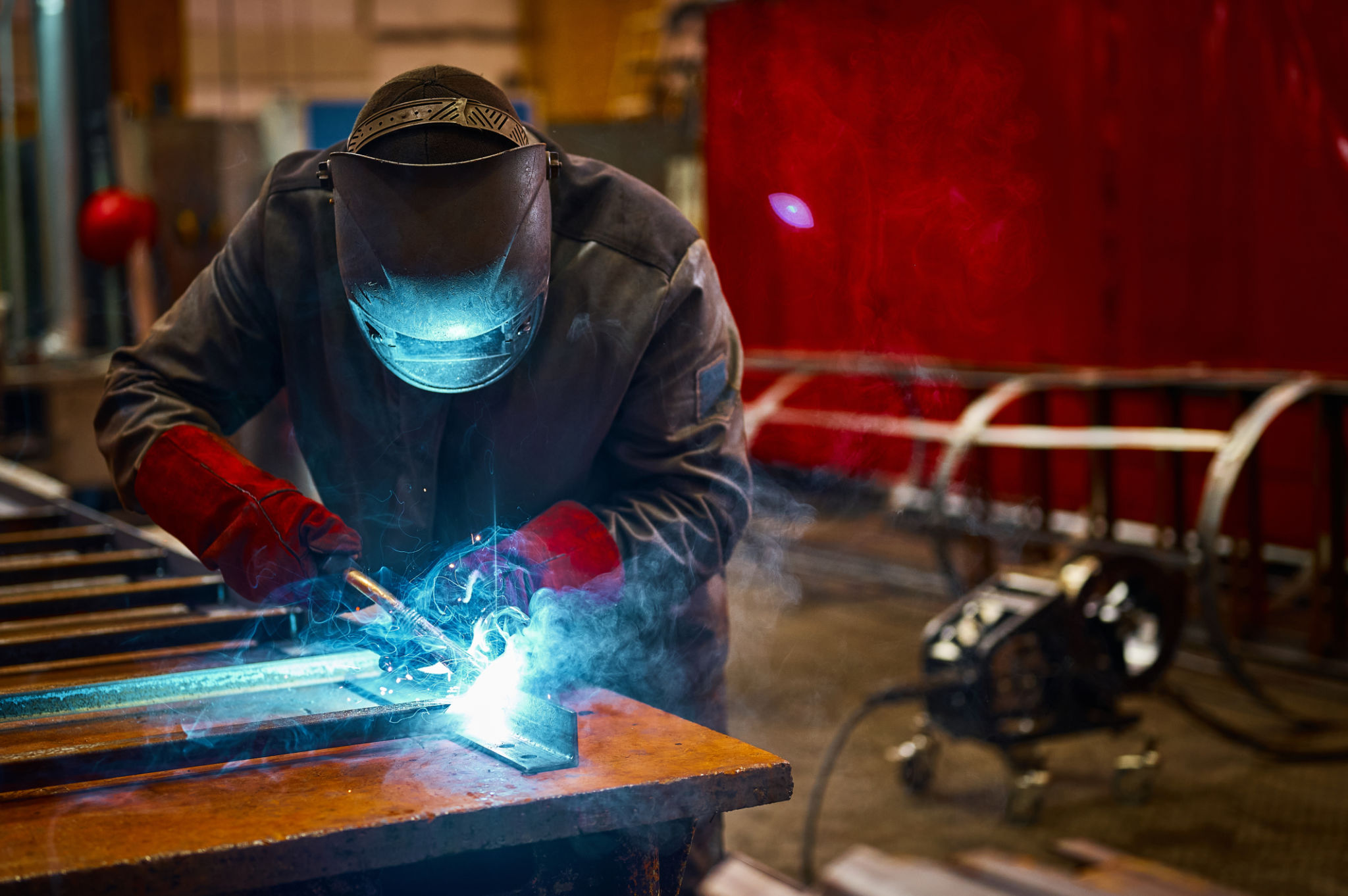 Skilled worker in protective mask welds metal part at plant Skilled worker in protective mask welds metal part at plant