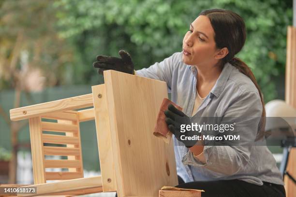 diligent female carpenter preparing a table to be painted or stained. young woodworker or craftswoman making furniture as hobby or to sell. serious woman sanding restored wood with sandpaper outside. - sandpapper bildbanksfoton och bilder