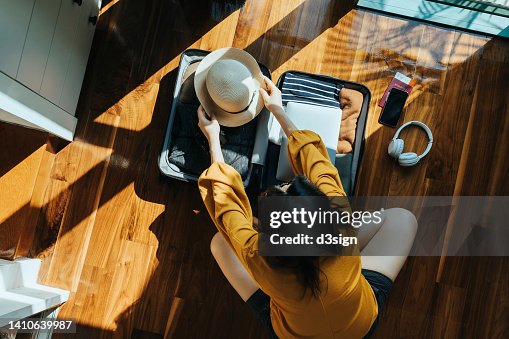 Overhead view of young Asian woman sitting on the floor in her bedroom, packing a suitcase for a trip. Getting ready for a vacation. Traveller's accessories. Travel and vacation concept Overhead view of young Asian woman sitting on the floor in her bedroom, packing a suitcase for a trip. Getting ready for a vacation. Traveller's accessories. Travel and vacation concept