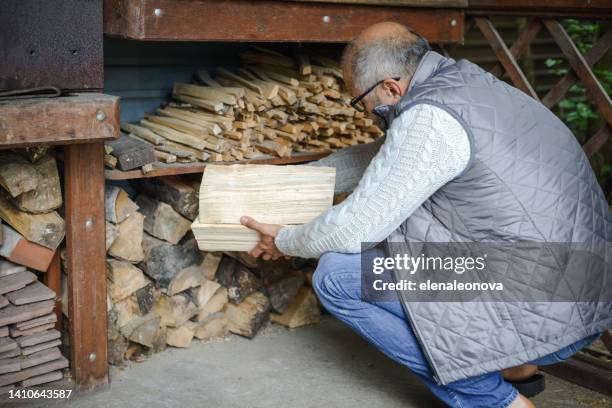 reifer erwachsener mann, der brennholz trägt - holzstapel stock-fotos und bilder