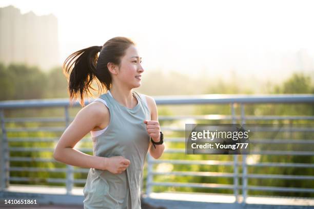 asiatische junge frau, die morgens auf der stadtstraße läuft - marathon läufer stock-fotos und bilder