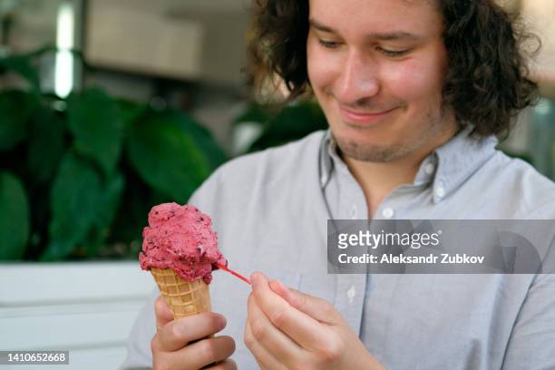 a young man, a guy eats ice cream in a cone in a cafe, cafeteria, in a chain of fast food restaurants. vegan ice cream in the hands of a high school student. berry sherbet, sweet dessert. the concept of rest and relaxation, vacations. dependence on sweets - georgian man stock pictures, royalty-free photos & images