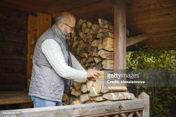 mature adult man carrying firewood - brandhout stockfoto's en -beelden