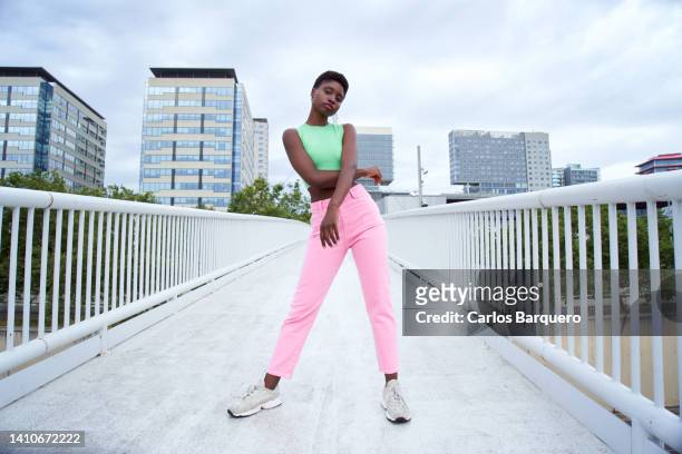 young african woman modelling to the camera while standing on a bridge and using colourful  clothes. - confident looking to camera stock pictures, royalty-free photos & images