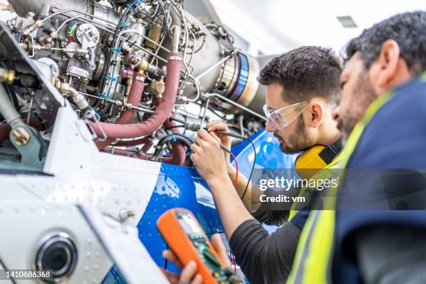 ingenieros aeronáuticos con chalecos reflectantes examinando el motor del helicóptero, utilizando multímetro, vista de cerca - fuselage fotografías e imágenes de stock