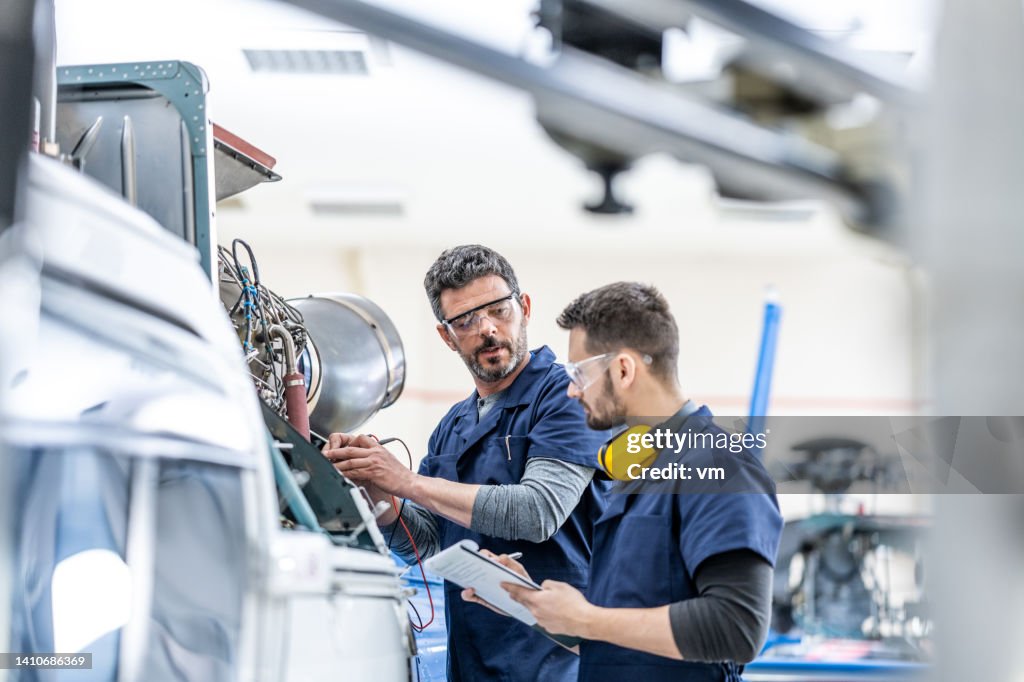 Young aviation mechanics studying to repair engine medium shot