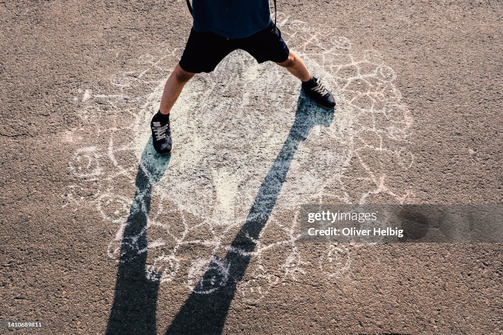 An unrecognizable boy stands on a chalk drawing which was painted on the street. The drawing symbolizes that we are all children of this earth.