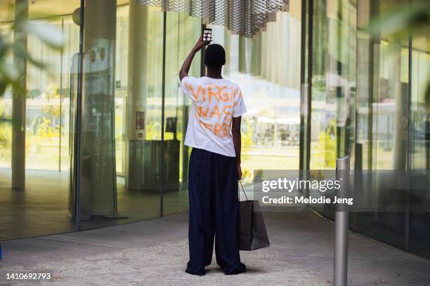 Model Gaye Serigne takes a photo on his iPhone and wears a Project Gaye Virgil Abloh graffiti "Virgil Was Here" t-shirt, blue pants at the Etro show...