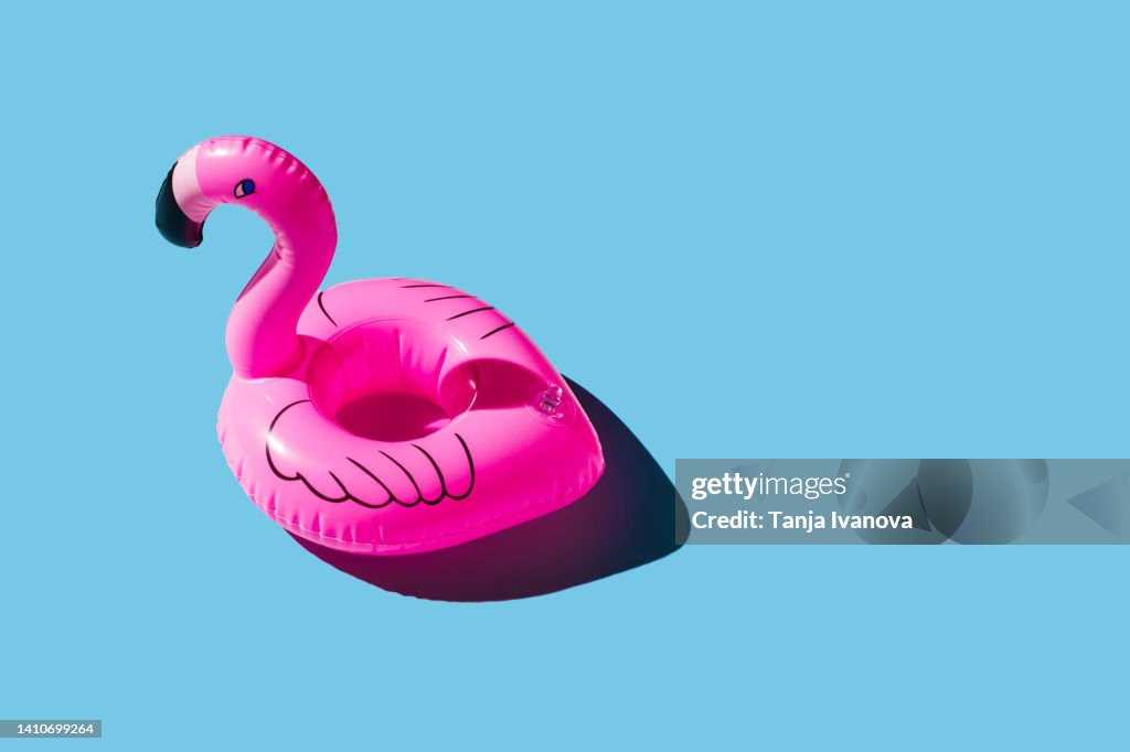 Pink inflatable flamingo on blue background. Summer holiday concept.