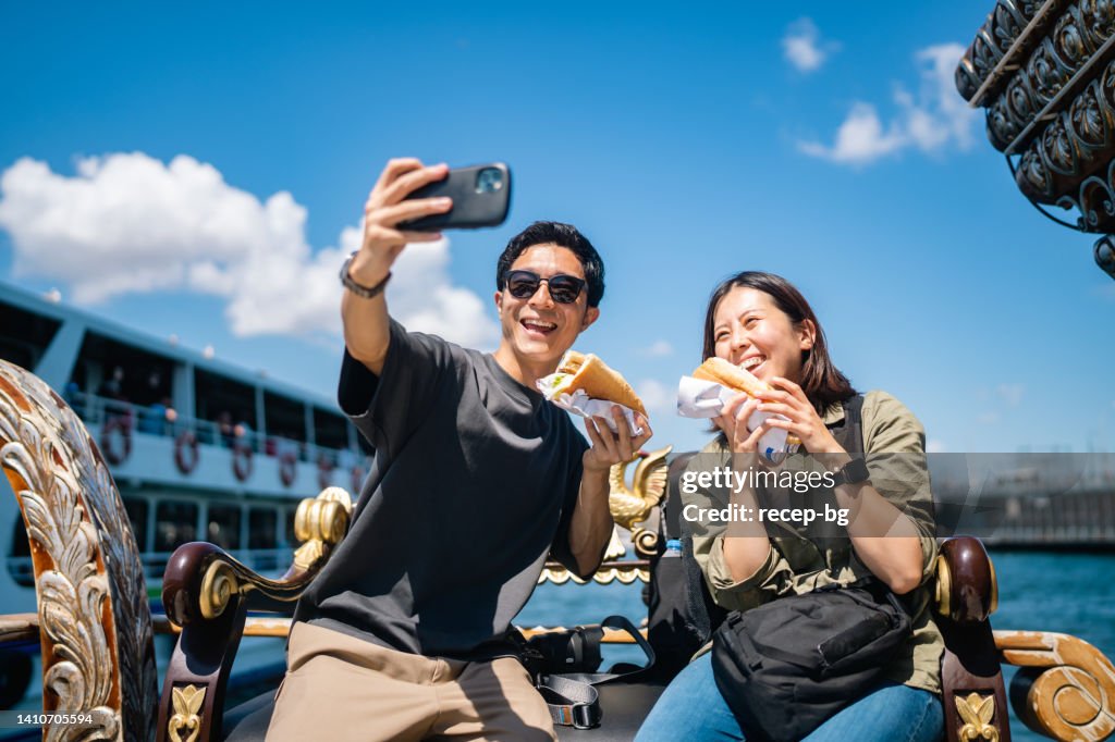Casal de turistas tirando selfie com telefone inteligente enquanto experimenta e come comida de rua durante sua viagem