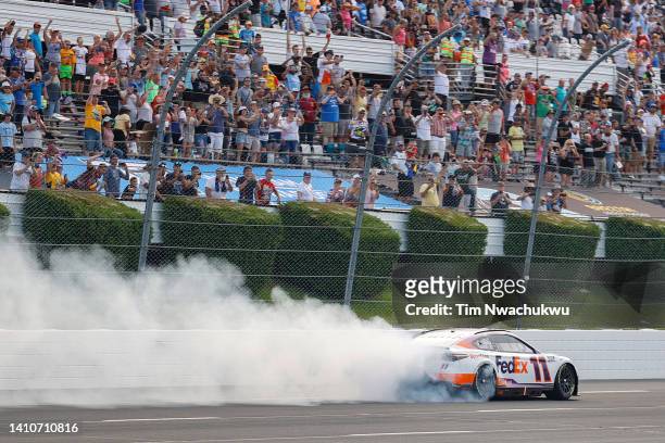 Denny Hamlin, driver of the FedEx Office Toyota, celebrates with a burnout after winning the NASCAR Cup Series M&M's Fan Appreciation 400 at Pocono...