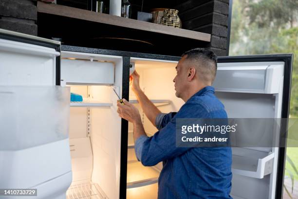 handyman fixing a fridge at a house - kitchen straighten stockfoto's en -beelden